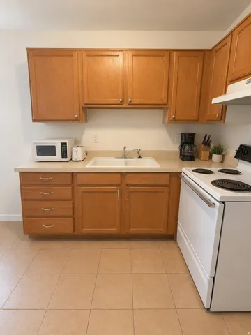Unit D: Kitchen featuring wood-finish cabinetry, solid surface countertops, a double basin sink with chrome faucet, a white electric range, and tiled flooring