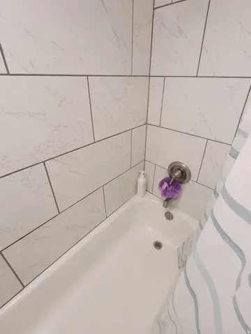 Unit B: Bathtub with a brushed nickel faucet and drain, surrounded by white tile with gray veining and dark grout