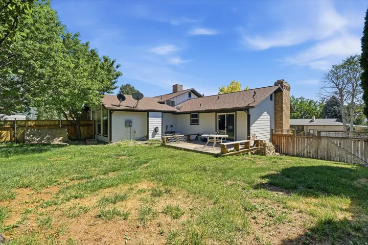 Expansive backyard featuring a wood privacy fence, mature trees, and a ground-level deck with sliding glass door access to the residence