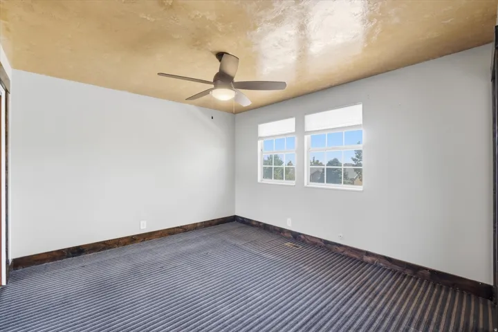 Interior room featuring light gray walls, a textured gold-finish ceiling, and a ceiling fan with integrated lighting
