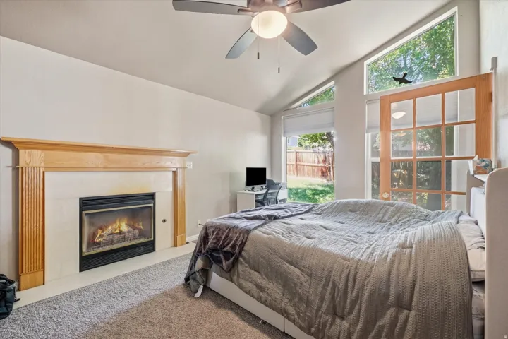 ADU Vaulted ceiling room featuring a natural wood mantel fireplace with a dark metal insert, multiple large windows, and a ceiling fan