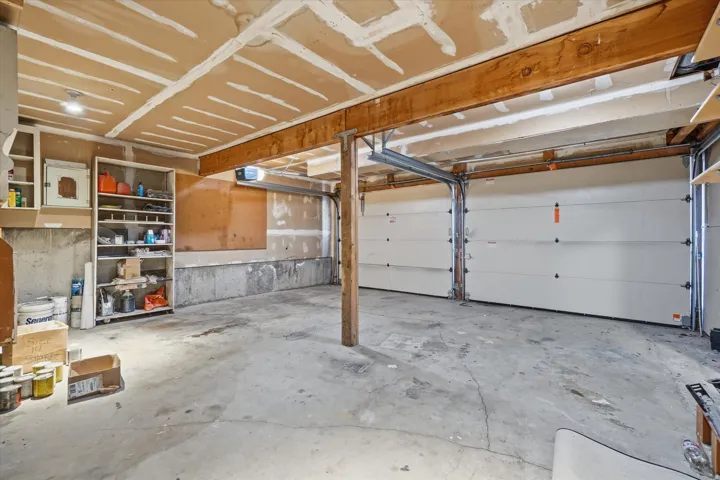 Spacious two-car garage featuring concrete flooring, exposed wood beams, and built-in shelving