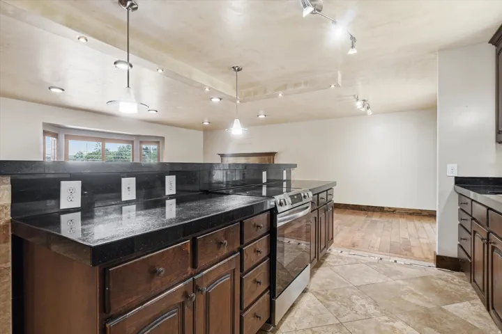 Kitchen featuring dark cabinetry, dark stone countertops, stainless steel range, ceramic tile flooring, and pendant lighting