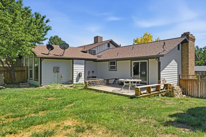 Expansive backyard featuring a wood deck, sliding glass door access, light-colored horizontal siding, and a brick chimney
