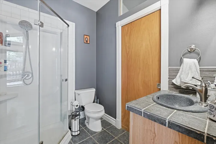 ADU  bathroom featuring a glass-enclosed shower with a multi-function showerhead, a single toilet, and a vanity with a tile countertop and integrated sink