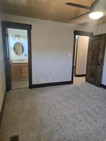 Plush carpeting throughout with dark wood trim, matching wood-paneled door, and a ceiling fan with integrated lighting