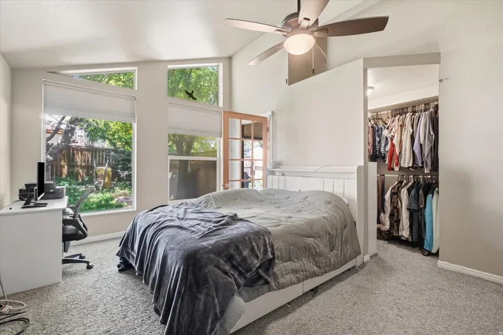 ADU Vaulted ceiling room featuring multiple windows with blinds, a ceiling fan, plush carpet flooring, and a walk-in closet with built-in shelving