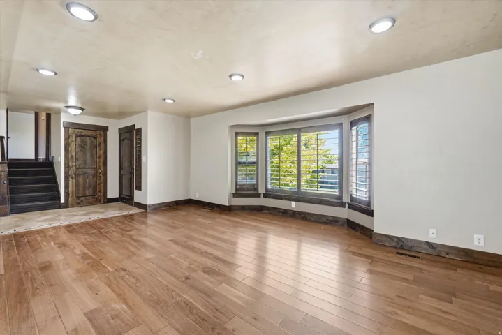 Spacious room featuring wood-finish flooring, a multi-panel bay window with plantation shutters, recessed lighting, and a textured ceiling