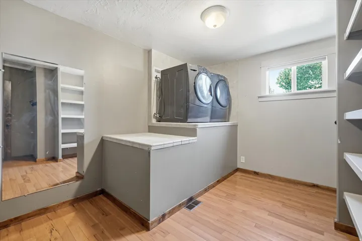 one of three Laundry areas featuring wood-finish flooring, a window, a built-in platform with a countertop, and wall-mounted shelving