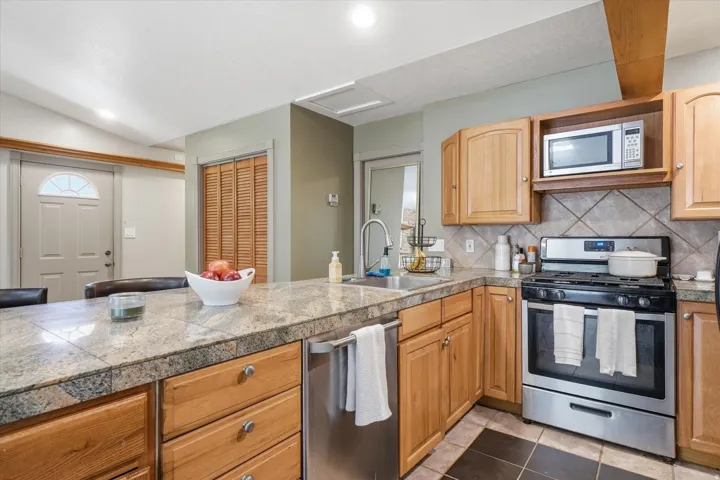 ADU Kitchen featuring granite countertops, wood cabinetry, stainless steel appliances, a tile backsplash, and dark tile flooring