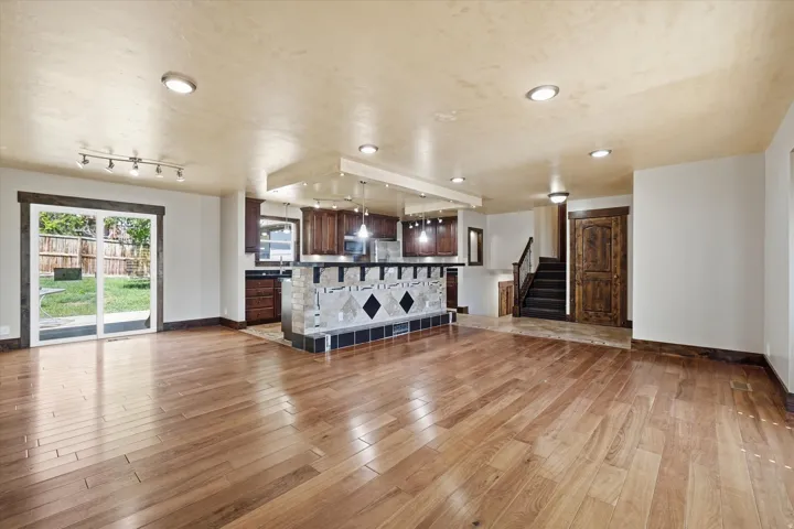 Spacious open-concept living area featuring wood-finish flooring, recessed lighting, and a sliding glass door to the backyard