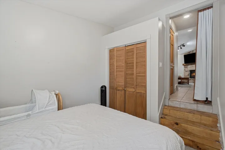 Room featuring louvered bi-fold closet doors and wood steps leading to an adjacent area with stone-finish fireplace