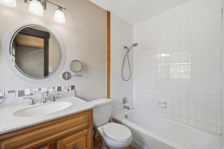 Bathroom featuring a wood vanity with a light-colored countertop, an oval mirror, and a full bathtub with white tile surround