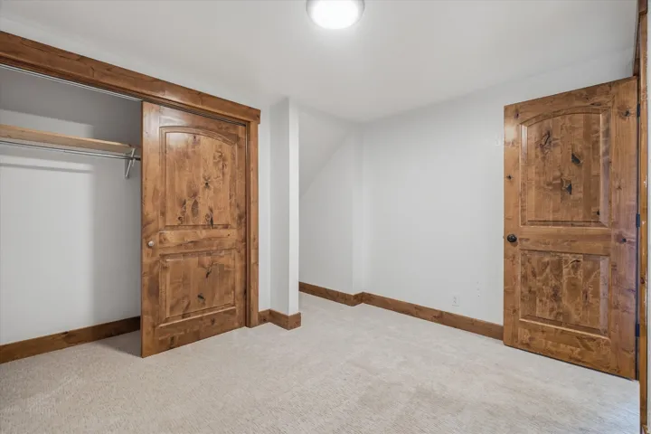 Bedroom featuring light-toned carpeting, white walls, and rich wood-paneled doors