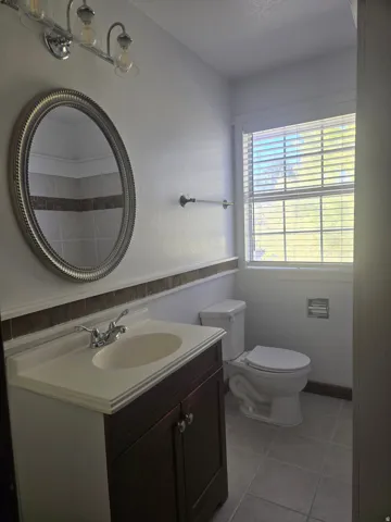 Bathroom featuring a wood-finish vanity with a single basin sink, tiled flooring, and a window with horizontal blinds