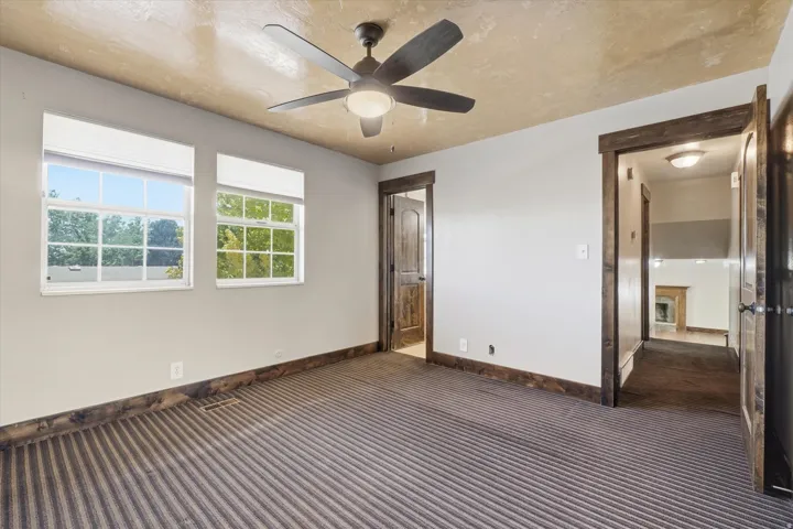 Room featuring striped carpeting, two windows with blinds, and a ceiling fan with integrated lighting