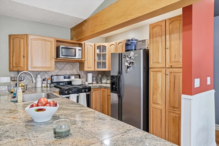 ADU Kitchen featuring granite countertops, wood cabinetry, stainless steel appliances, and a tile backsplash