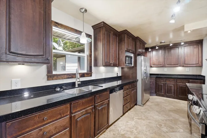 Kitchen featuring dark wood cabinetry, black countertops, stainless steel appliances, and tile flooring