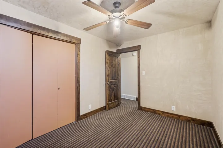 Room featuring a ceiling fan with light fixture, textured walls, wood-finish trim, and striped carpeting