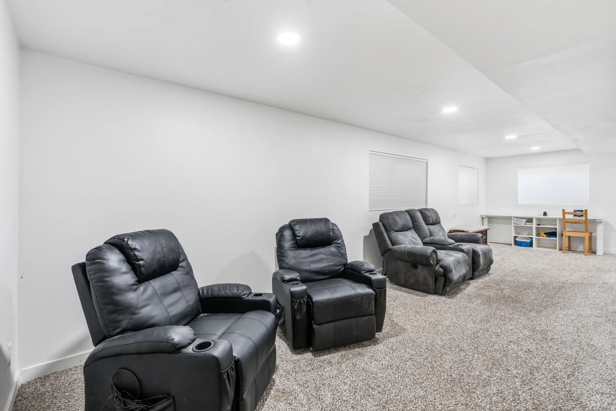 Spacious room featuring light gray carpet, white walls, recessed ceiling lighting, and built-in shelving with a white countertop