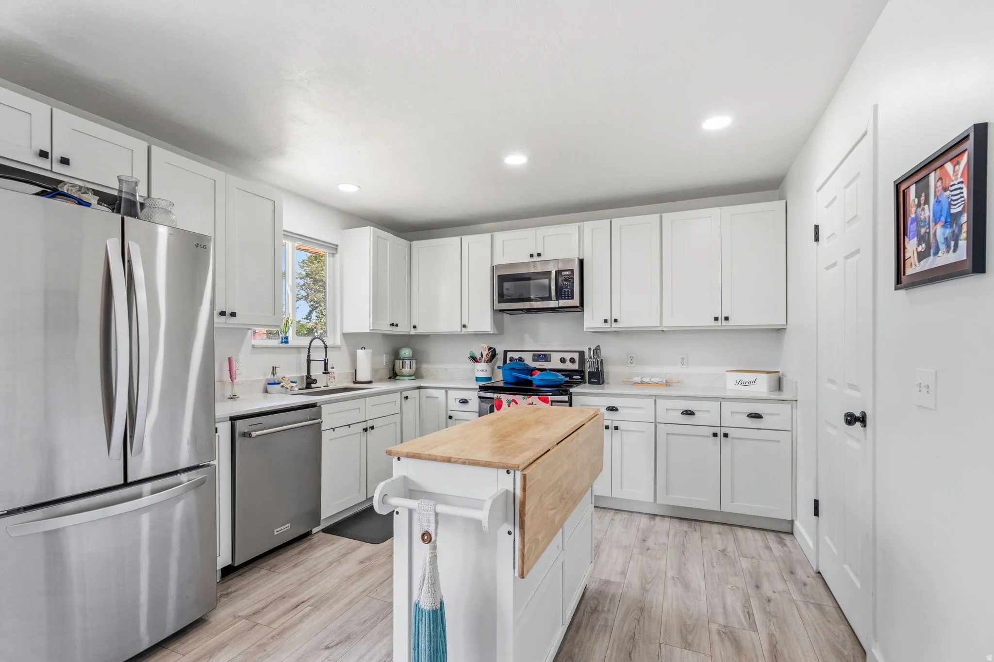 White kitchen featuring a full suite of stainless steel appliances, shaker-style cabinetry, and wood-finish flooring