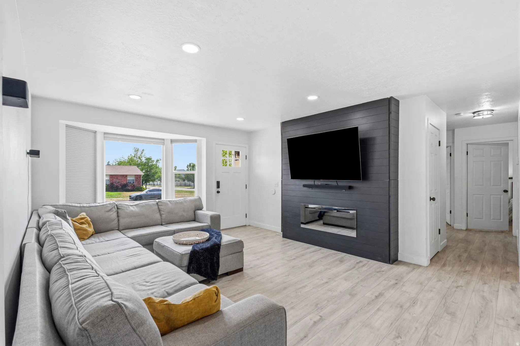Spacious living area featuring a modern accent wall with a built-in media center, wood-finish flooring, recessed lighting, and a front entry door with decorative glass