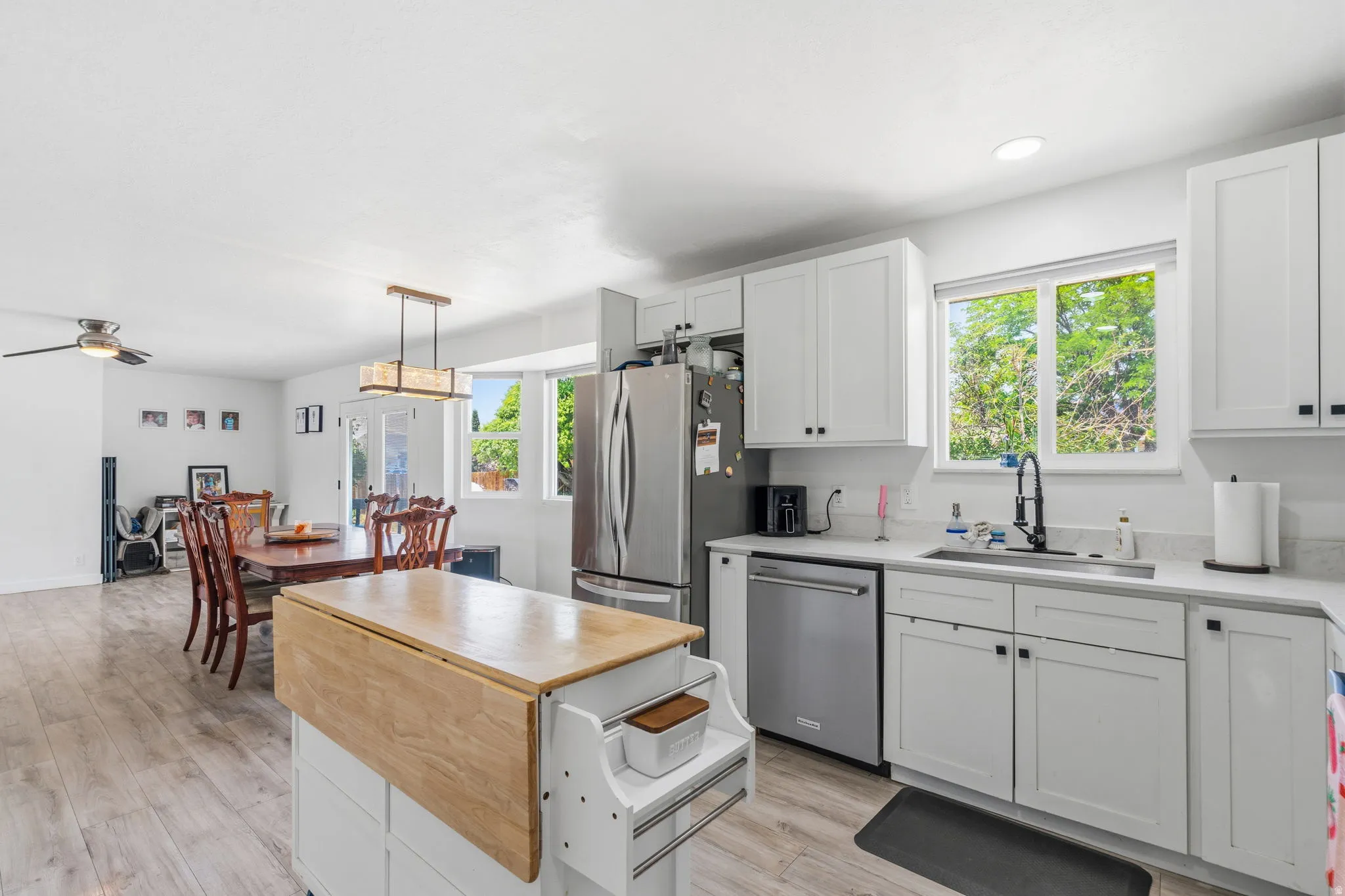 Kitchen and dining area featuring white cabinetry, stainless steel appliances, wood-finish flooring, a kitchen island with a wood countertop, and a contemporary ceiling fixture