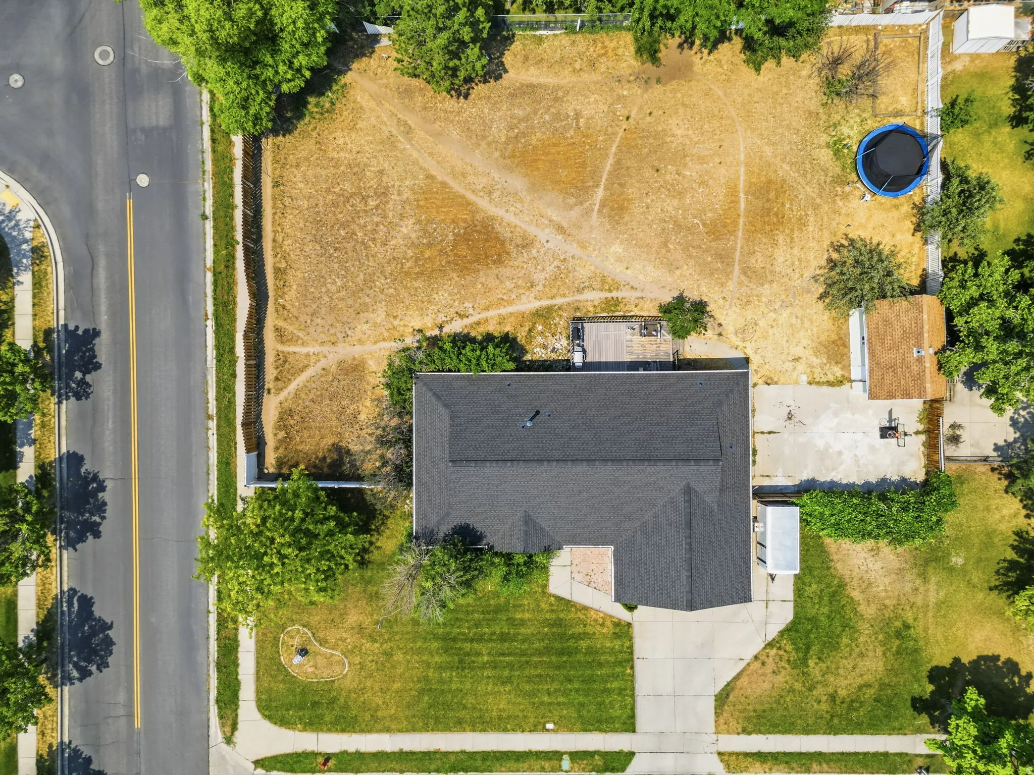 Expansive lot featuring a main residence with a dark shingle roof, a detached structure with a light-colored roof, and a large concrete driveway