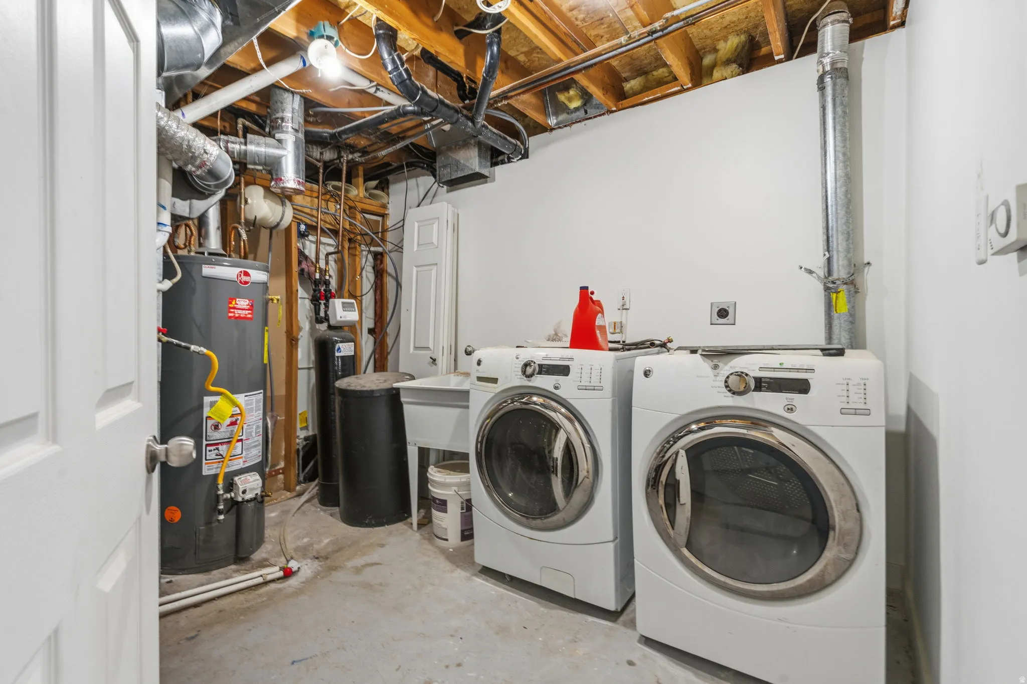 Utility area featuring laundry appliances, a water heater, and an exposed ceiling