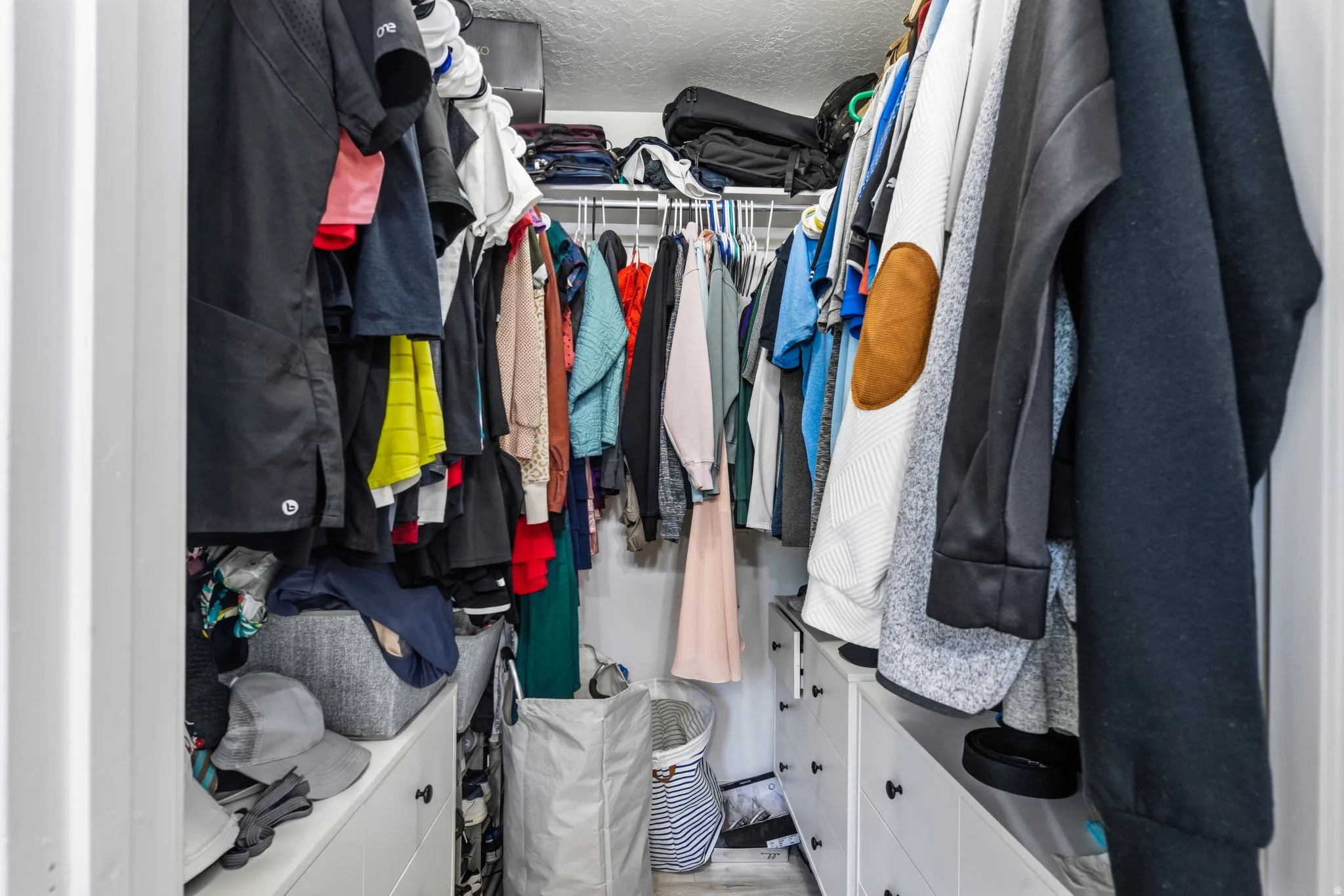 Walk-in closet featuring built-in white cabinetry, black hardware, wire shelving, and light wood-finish flooring