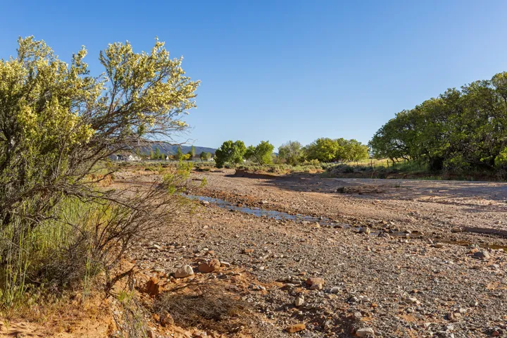 Rocky terrain featuring a narrow stream bed, surrounding greenery, and distant residential structures