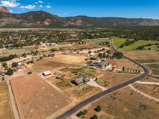 Expansive rural property featuring a large residence with a multi-car garage, a red barn, and a fenced paddock area