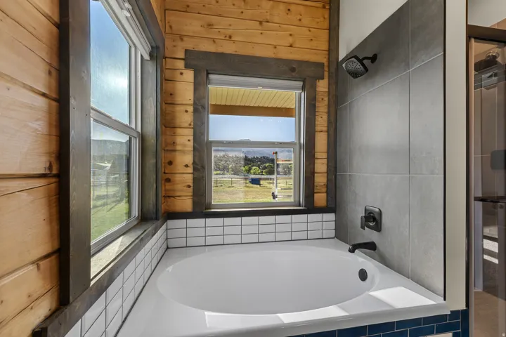 Built-in soaking tub with matte black fixtures, white subway tile surround, and blue accent tiling