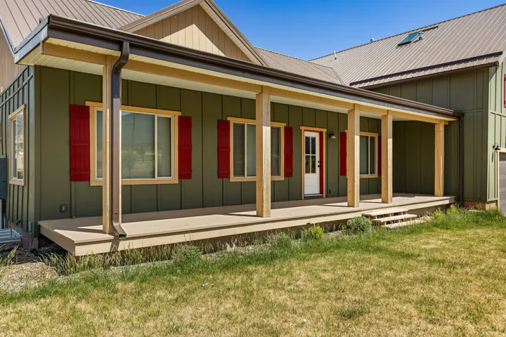 Covered front porch with wood-finish columns, board and batten style siding, red window shutters, a white paneled entry door, and a metal roof