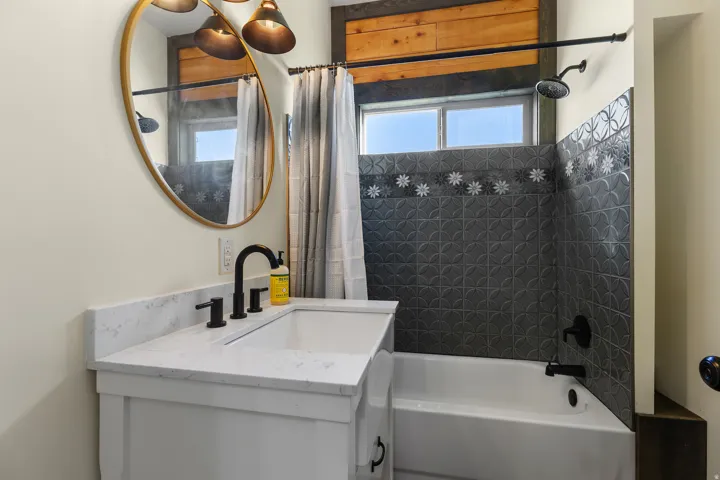 Bathroom featuring a white vanity with a white countertop, matte black fixtures, an oval mirror, and a tiled shower-bath combination with a decorative border