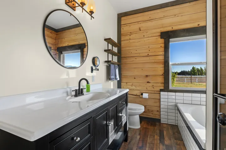 Bathroom featuring a dark wood vanity with a white countertop, oval mirror, and wall-mounted light fixture