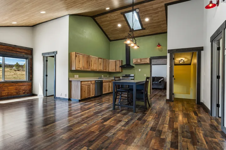 Open-concept kitchen and living area featuring wood-finish flooring, a vaulted wood-paneled ceiling with recessed lighting, and a skylight