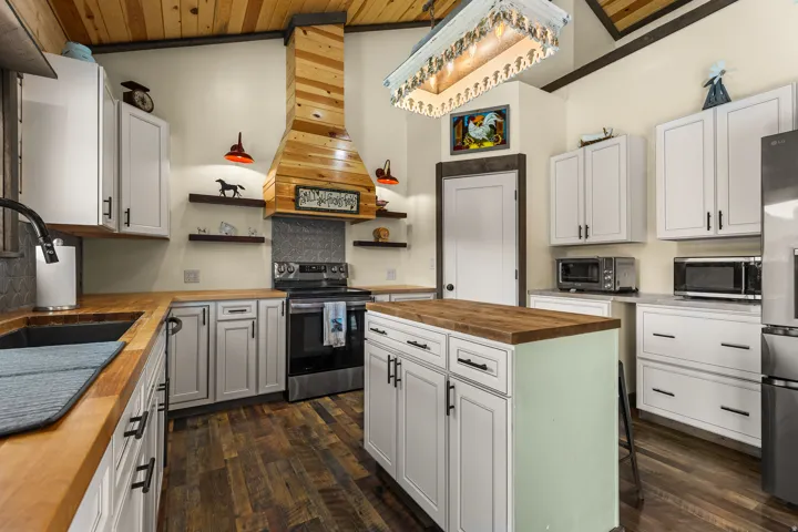 Kitchen featuring wood-finish flooring, white cabinetry, solid wood countertops, a central island with storage, and a custom wood range hood
