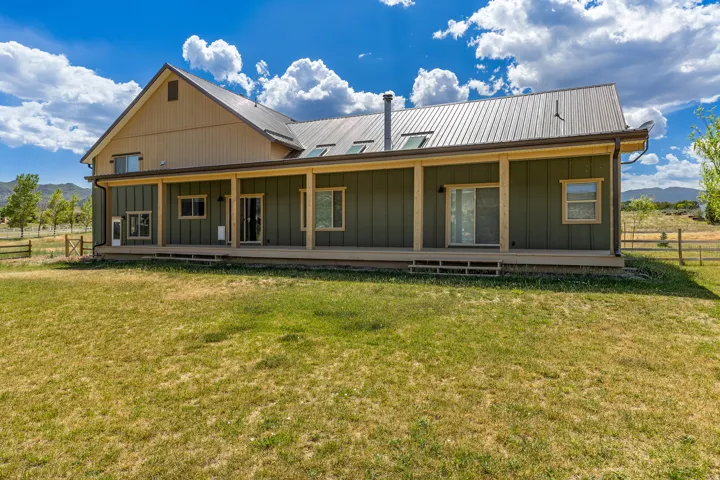 Expansive rear elevation featuring a covered porch, multiple sliding glass doors, and a durable metal roof