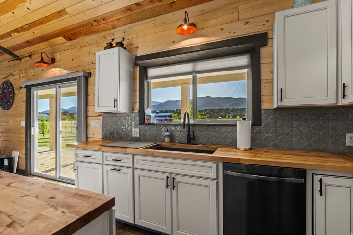 Kitchen featuring wood-finish paneling, white cabinetry with black hardware, wood-finish countertops, black sink with a matte black faucet, and a patterned tile backsplash
