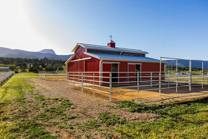 Red barn structure featuring a metal roof, cupola with weather vane, and attached metal corrals