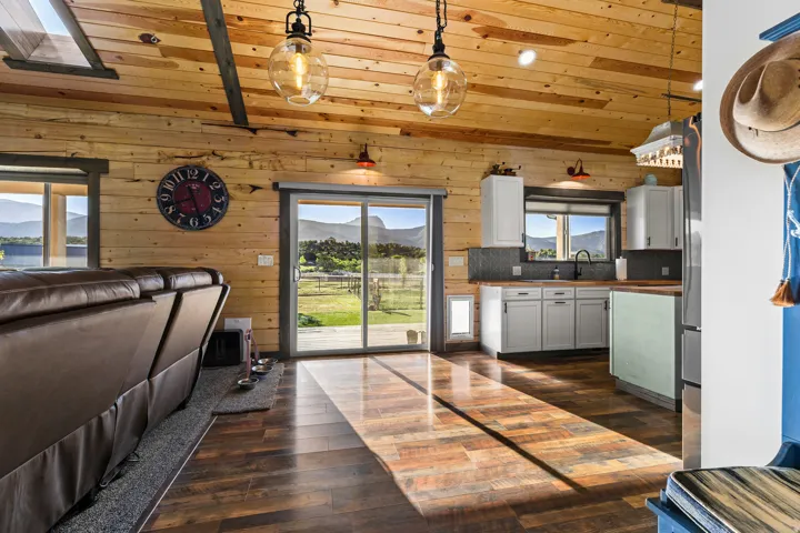 Open-concept living space featuring wood-finish flooring, natural wood plank walls, and a matching wood plank ceiling with exposed beams