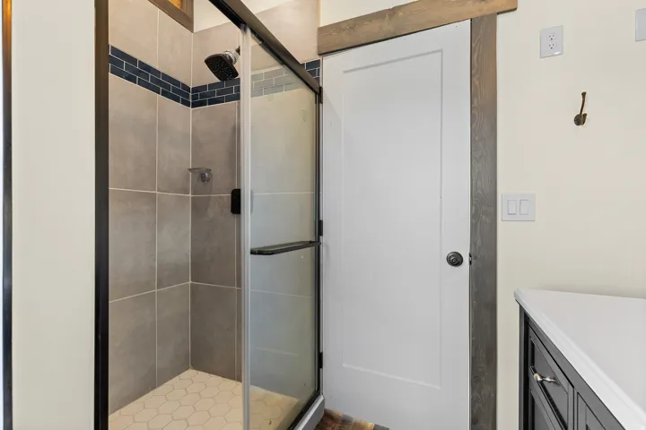 Shower enclosure with gray wall tiles, a blue mosaic accent band, and a hexagonal floor tile pattern