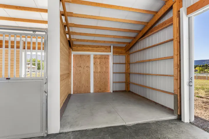 Spacious interior barn area featuring concrete flooring and exposed wood ceiling trusses