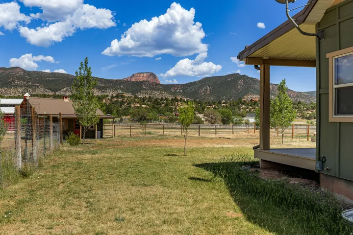 Expansive grassy yard with mountain scenery, featuring a covered patio, a separate outbuilding with a metal roof, and perimeter fencing