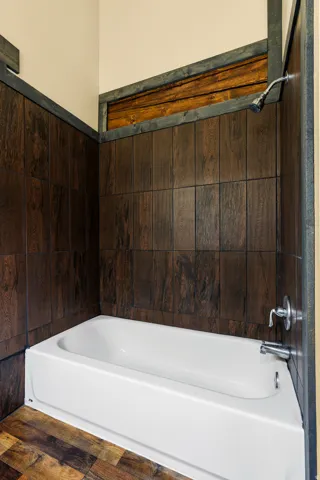 White bathtub with chrome fixtures, surrounded by dark wood-finish wall paneling and a rustic wood accent band