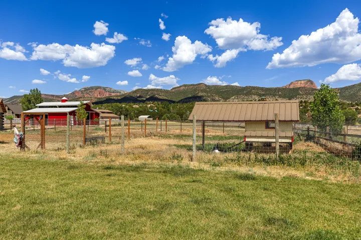 Fenced outdoor area featuring a red barn, an outbuilding with a metal roof, and distant mountains
