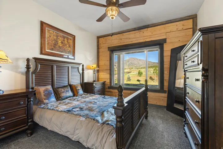 Bedroom featuring a large window, wood-paneled accent wall, a ceiling fan with integrated lighting, and carpet flooring