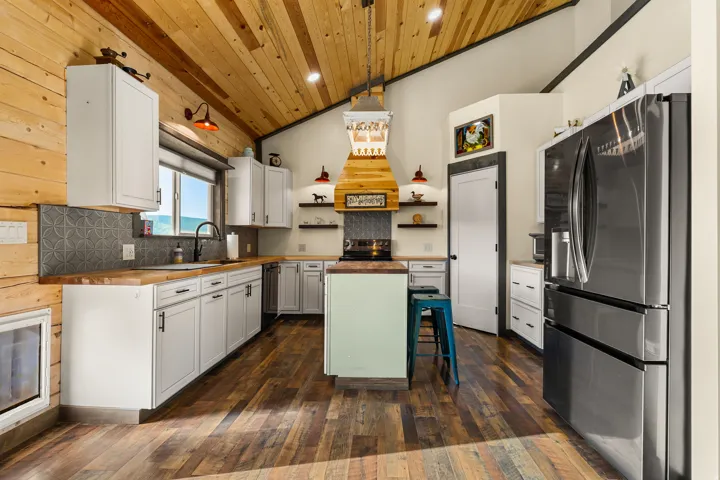 Open-concept kitchen with vaulted wood-plank ceilings, wood-finish flooring, white cabinetry, and stainless steel appliances