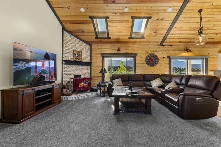 Living area featuring vaulted wood-plank ceilings, two skylight windows, and a corner brick fireplace with a red wood-burning stove
